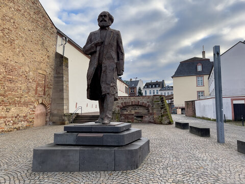 View of the Karl Marx statue standing in a cobblestone square with historic brick walls and urban buildings in the background in Trier, Rheinland-Pfalz, Germany.