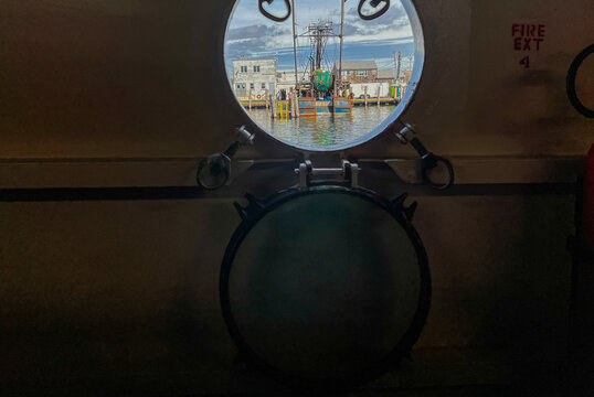 View of a fishing boat docked in the harbor as seen through a circular ship porthole on Block Island in New Shoreham, Rhode Island, United States.