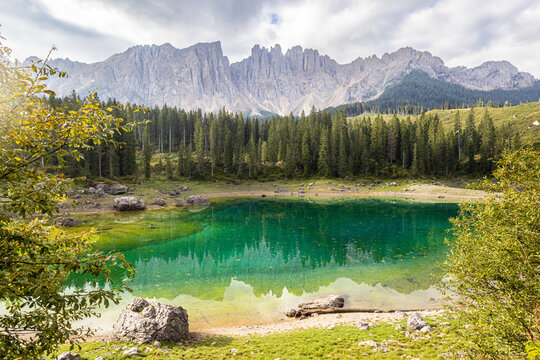 View of Karersee with vibrant emerald green water reflecting the dense coniferous forest and jagged Latemar mountain peaks in Welschnofen, Trentino-Alto Adige, Italy.