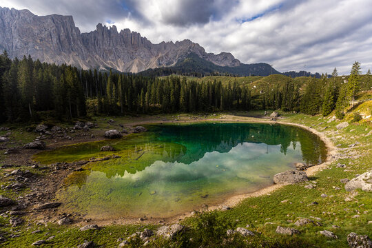 View of the emerald waters of Karersee reflecting the jagged peaks of the Latemar mountain range and surrounding pine forest in Welschnofen, Trentino-Alto Adige, Italy.