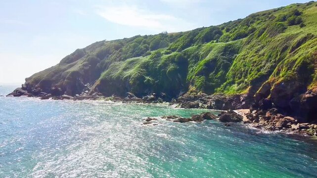 Aerial view of Lantic Bay with lush green cliffs meeting the turquoise sea along the rocky coastline in Polruan, United Kingdom.
