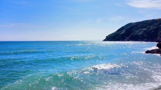 Aerial view of Lantic Bay with rocky cliffs, sandy beach, and turquoise sea under a clear blue sky in Polruan, United Kingdom.
