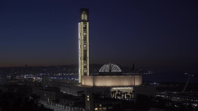 Aerial view of the illuminated Great Mosque of Algiers with its tall minaret and dome glowing against the dark night sky in Algiers, Algeria.