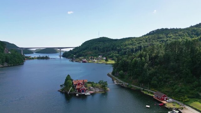 Aerial view of the small island of Sogne with traditional red cabins surrounded by calm fjord waters and lush green hills in Kristiansand, Agder, Norway.