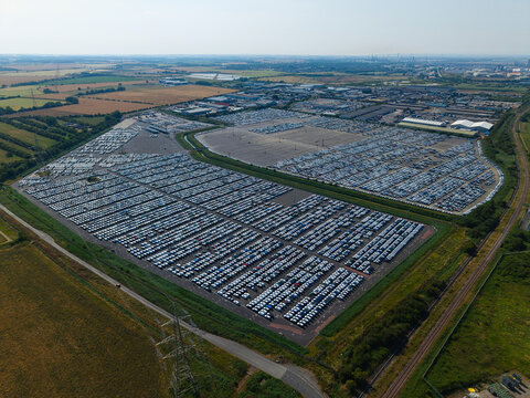 Aerial view of the BCA Kia car distribution center featuring thousands of new vehicles parked in organized rows across a large asphalt lot in Stallingborough, England, United Kingdom.