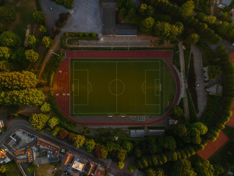 Aerial view of a soccer field with a running track surrounded by lush trees and nearby buildings in Antoing, Region wallonne, Belgium.