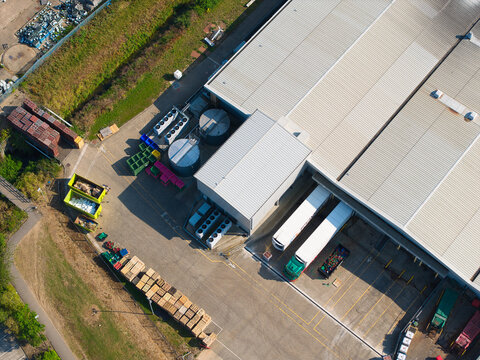 Aerial view of a large industrial warehouse facility with trucks parked at loading bays, storage tanks, and pallets in the yard in Grimsby, England, United Kingdom.