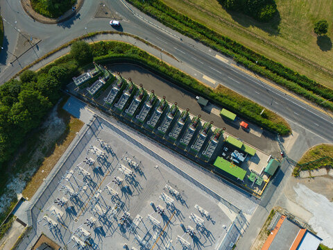 Aerial view of an electrical substation with containerized industrial generator compressor units, adjacent to a road and green surroundings in Immingham, England, United Kingdom.