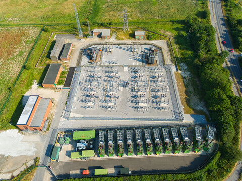 Aerial view of an electrical substation featuring rows of containerized industrial generator compressor units and power transformers in a fenced facility in Immingham, England, United Kingdom.
