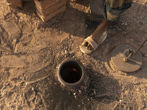 Chattogram, Chittagong Division, Bangladesh - 07 February 2026: View of a person standing near a traditional ground-level fire pit used for cooking in a dusty outdoor setting.