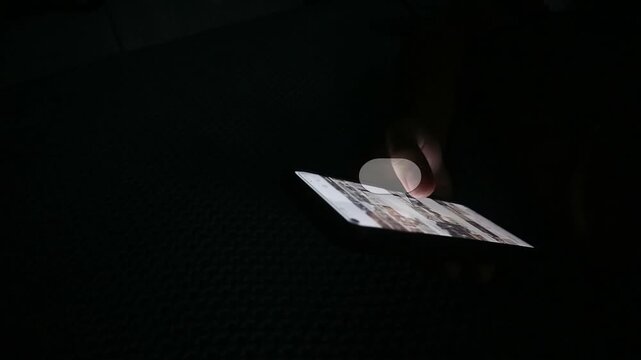 Person using a smartphone screen in a dark room at night.