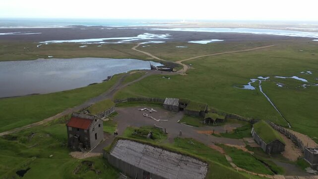 Aerial view of the historic Viking village set with turf-roofed buildings and wooden structures surrounded by green grassy plains at Myrdalshreppur, Iceland.