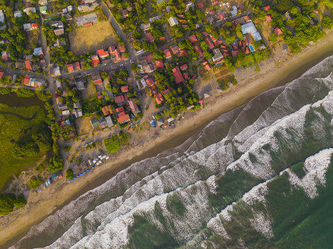 Aerial view of the coastal town of Ayampe, featuring red-roofed houses, lush green vegetation, and the sandy beach meeting the Pacific Ocean in Ayampe, Manabi, Ecuador.