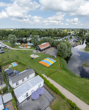 Aerial view of De Holle Poarte holiday park featuring a large inflatable jumping pillow, playground, canal, and chalets in Makkum, Friesland, Netherlands.