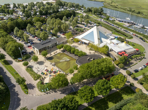Aerial view of De Holle Poarte recreational area with its pyramid-shaped building, central pond, fountain, trees, and parking lot in Makkum, Friesland, Netherlands.
