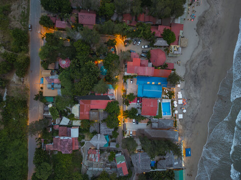 Aerial view of Montanita beach town featuring colorful rooftops, lush tropical trees, swimming pools, and a coastal road illuminated at dusk in Montanita, Santa Elena, Ecuador.