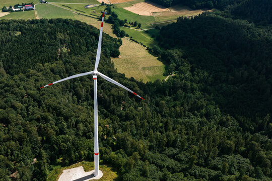Aerial view of a wind turbine standing in a dense green forest with agricultural fields in the background in Burghaun, Hessen, Germany.
