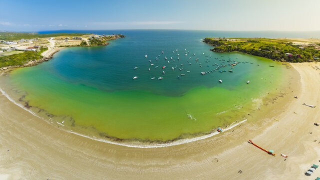 Aerial view of the turquoise waters of Ayangue Bay filled with small fishing boats, surrounded by sandy beaches and coastal cliffs in Ayangue, Santa Elena, Ecuador.
