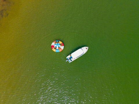 Aerial view of a small white boat and a colorful inflatable water toy with people floating on the green waters of Ayangue, Santa Elena, Ecuador.