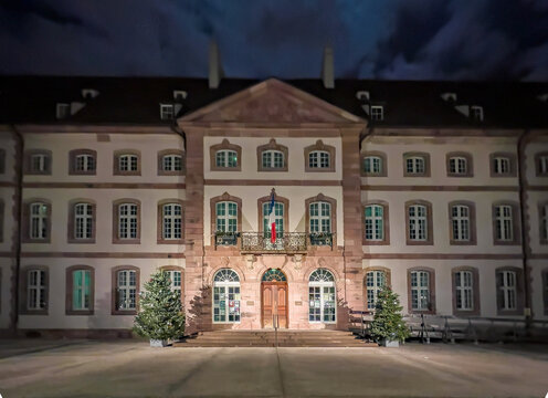 View of the historic Unterlinden Museum building illuminated at night with Christmas trees and a French flag on the balcony in Colmar, Grand Est, France.