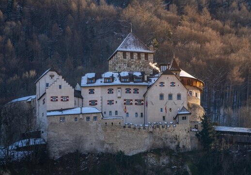 View of Vaduz Castle with its medieval stone walls and snow-covered rooftops nestled against a forested hillside during the golden hour in Vaduz, Vaduz, Liechtenstein.