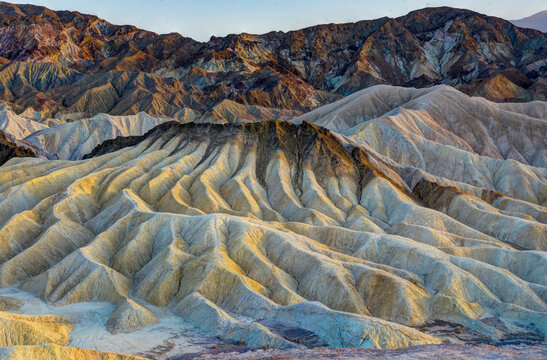 View of the rugged, eroded badlands of Death Valley National Park with colorful sedimentary layers and dramatic shadows in Death Valley, California, United States.