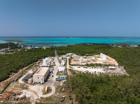 Aerial view of an industrial facility with power stations, fuel and storage tanks surrounded by lush green vegetation near turquoise waters in George Town, Exuma, The Bahamas.