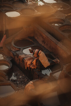 Fes, Morocco - 11 November 2025: View of a worker processing leather in the historic Chouara Tannery with traditional stone vats filled with dye under warm golden light.
