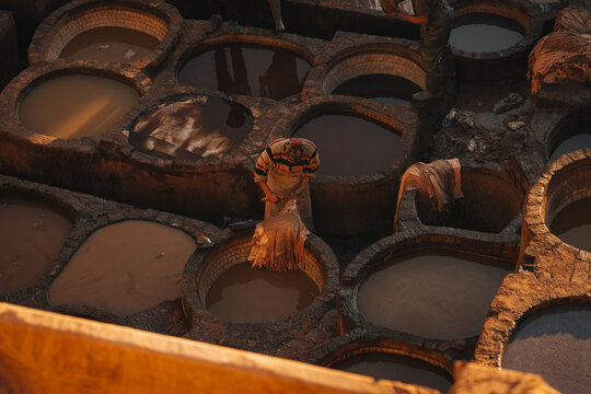 Fes, Morocco - 11 November 2025: View of the historic Chouara Tannery with workers processing leather in traditional stone dye vats under warm sunlight.
