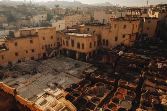 Fes, Morocco - 11 November 2025: View of the historic Chouara Tannery with workers processing leather in stone vats surrounded by traditional buildings.
