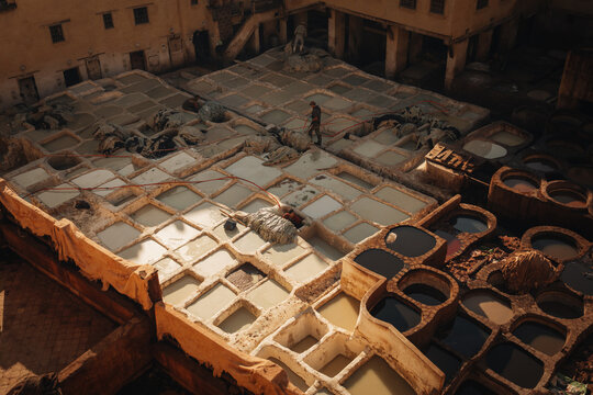 Fes, Morocco - 11 November 2025: View of the historic Chouara Tannery with workers processing leather in stone dye vats surrounded by traditional buildings.