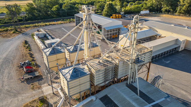 Aerial view of a grain storage and processing facility featuring metal silos, bucket elevators, and industrial buildings in a rural setting in Saulce-sur-Rhone, Auvergne-Rhone-Alpes, France.