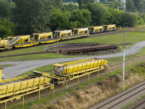 Aerial view of a train repair station with yellow maintenance wagons on tracks and a railway turntable surrounded by green trees in Krakow, Lesser Poland Voivode, Poland.