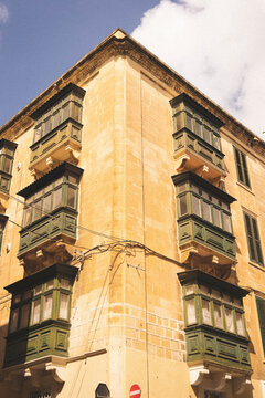 Valletta, Malta - 14 July 2022: View of traditional Maltese wooden balconies on a historic limestone building in the city center under a clear blue sky.