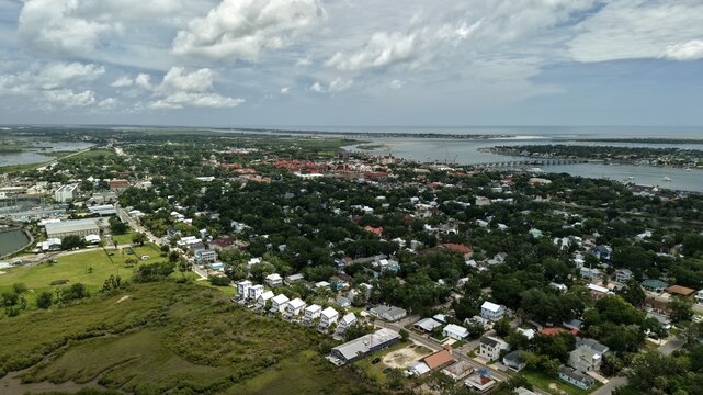 Aerial view of the historic city of St. Augustine featuring lush green trees, residential rooftops, the Matanzas River, and the Bridge of Lions in St. Augustine, Florida, United States.