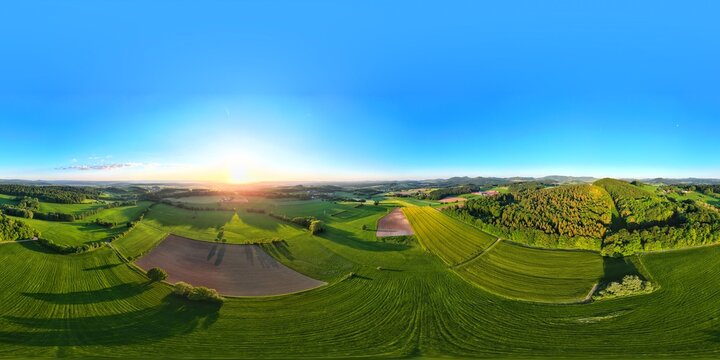 Aerial view of the Rhon Mountains landscape near Fulda, featuring rolling green hills, agricultural fields, and forests under a clear blue sky at sunset in Fulda, Hessen, Germany.