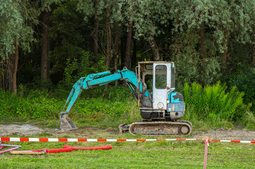 Small mini excavator preparing ground land plot for house construction near forest. Land clearing, excavation work and site preparation © Gereish