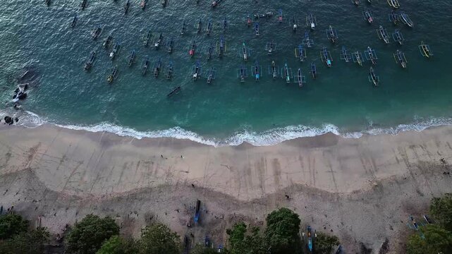 Aerial view of Papuma Beach featuring numerous traditional fishing boats anchored in turquoise waters along the sandy coastline in Jember, East Java, Indonesia.