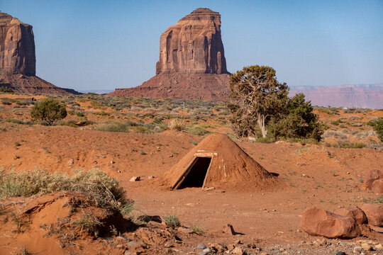 View of a traditional Navajo hogan set against the iconic red sandstone buttes of Monument Valley Tribal Park in the desert landscape of Oljato-Monument Valley, Utah, United States.