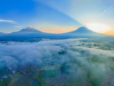 Aerial view of the Semayu mountains rising above a sea of clouds with lush terraced rice fields in the valley below at sunrise in Selomerto, Central Java, Indonesia.