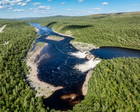 Aerial view of Pikefossen falls with its cascading water flowing through the lush green forests and rocky landscape of Kautokeino, Finnmark, Norway.