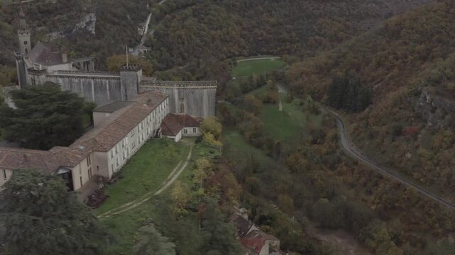 Aerial view of historic sanctuary buildings with stone walls and tiled roofs nestled in the lush valley of Rocamadour, Occitanie, France.
