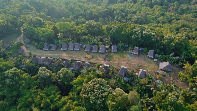 Aerial view of traditional thatched-roof houses of Kampung Adat Belaraghi nestled within lush tropical forest in Kecamatan Aimere, Nusa Tenggara Timur, Indonesia.