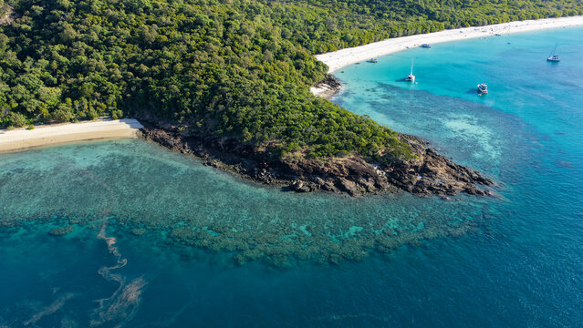 Aerial view of Whitehaven Beach featuring pristine white sand, turquoise waters, coral reefs, and lush tropical forest with boats anchored in the Whitsundays, Queensland, Australia.