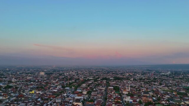 Aerial view of the city of Malang at sunset with a colorful sky over dense residential rooftops in Malang, East Java, Indonesia.