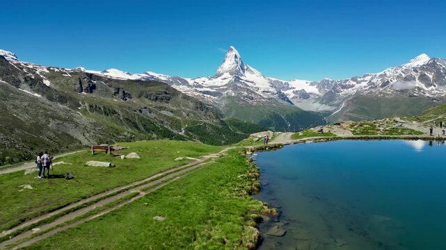 Aerial view of Matterhorn reflected in the clear waters of Stellisee lake surrounded by alpine meadows and snow-capped peaks in Zermatt, Valais, Switzerland.