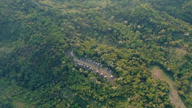 Aerial view of the traditional Kampung Adat Belaraghi village surrounded by dense forest and rolling hills in Kecamatan Aimere, Nusa Tenggara Timur, Indonesia.
