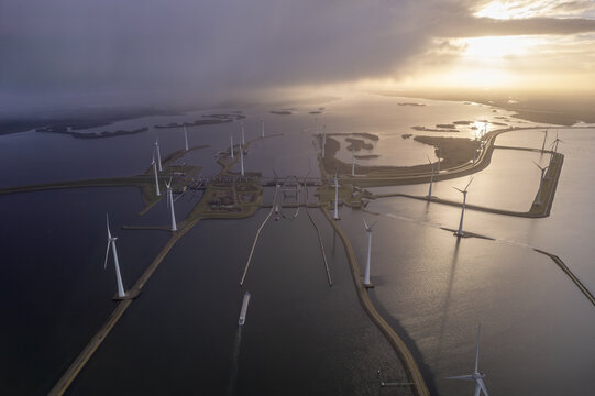 Aerial view of the Krammer locks featuring wind turbines, water channels, and a cargo ship navigating the waterway under a dramatic sunset sky in Bruinisse, Zeeland, Netherlands.