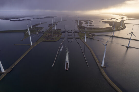 Aerial view of the Krammer locks featuring a cargo ship navigating the waterway surrounded by wind turbines under a dramatic sky in Bruinisse, Zeeland, Netherlands.