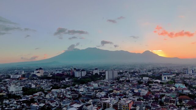 Aerial view of Malang city skyline at sunset with Gunung Butak, Gunung Kawi, and Gunung Panderman as one called Barisan Putri Tidur in the background in Malang, East Java, Indonesia.